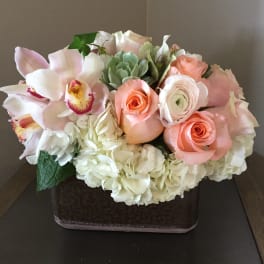 Pastel bouquet with roses, orchids, hydrangeas, and a succulent in a square vase