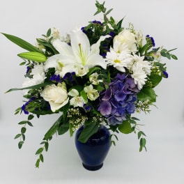 White and purple mixed flower arrangement in a navy blue vase