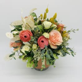 Peach and coral roses with white blooms arranged in a decorative ceramic pot.