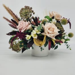 Low arrangement of blush roses, white blooms and textured accents in a white cylinder vase