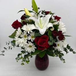 Red roses, white lilies, and white daisy mums arranged in a red glass vase