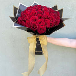 Arm holding a large bouquet of red roses wrapped in black paper with a gold bow.