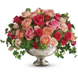 Low arrangement of pink and peach roses with trailing ivy in a silver pedestal bowl.