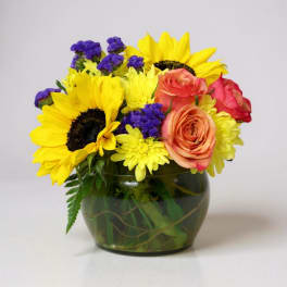 Bouquet of sunflowers, roses, and purple filler flowers in a glass vase