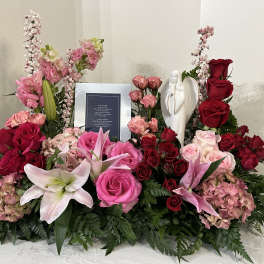 Large floral sympathy arrangement with pink and red roses, lilies, and an angel figurine