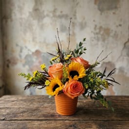 Orange roses and sunflowers arranged in a small terracotta pot