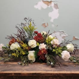 Low floral arrangement with white roses, red mums, and dark foliage