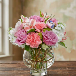 Round arrangement of pink and lavender roses, pink carnations, and white blooms in a clear glass bowl vase