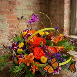 Orange and purple floral arrangement with butterfly decorations in a low container