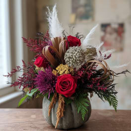Arrangement of red roses and purple flowers in a gray pumpkin vase