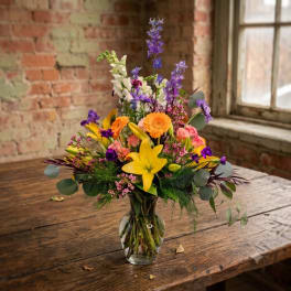 Mixed bouquet of yellow lilies, orange and pink blooms in a clear glass vase