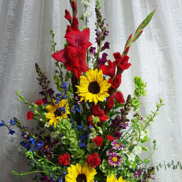 Tall mixed bouquet with sunflowers, red gladiolus, and blue flowers in a white vase