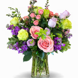Mixed roses and purple flowers arranged in a clear glass vase