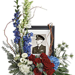 Floral tribute around a framed portrait with red, white, and blue flowers