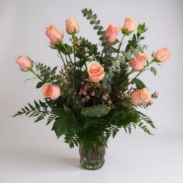 Pink roses arranged in a clear glass vase with mixed greenery