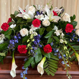 Casket spray with white lilies, roses, red carnations, and blue flowers
