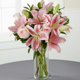 Pink lilies and roses arranged in a clear glass vase