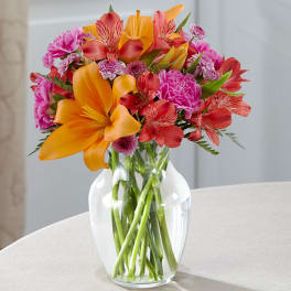 Bright mixed bouquet of orange, red, and pink flowers in a clear glass vase