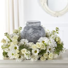 White roses and daisies arranged around a gray urn.