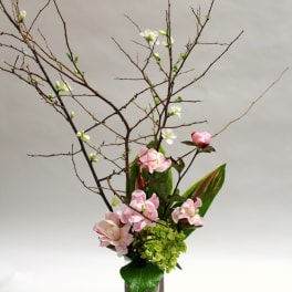Tall floral arrangement with pink blossoms and branching twigs in a glass vase