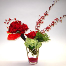 Red roses arranged in a clear glass vase with green hydrangea and decorative branches