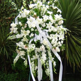 Large white funeral spray on a stand with ribbon streamers