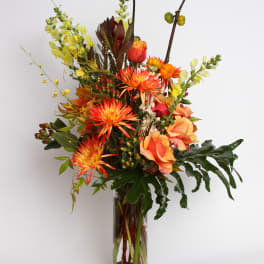 Tall mixed bouquet in a clear glass vase with orange and yellow blooms