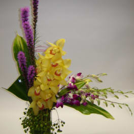 Yellow orchids and purple flowers in a clear glass vase