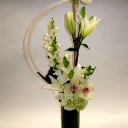 Tall white floral arrangement with lilies and orchids in a black vase