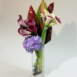 Purple calla lilies and a lavender hydrangea in a clear glass vase