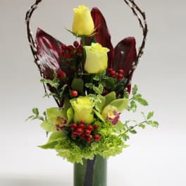 Yellow roses and green orchids in a tall vase with a decorative branch handle