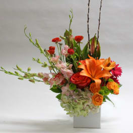 Colorful floral arrangement in a white rectangular vase with orange and pink blooms