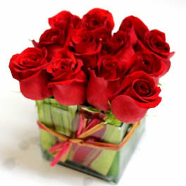Red roses arranged in a square glass vase with a ribbon tie