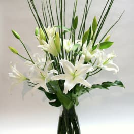 White lilies arranged in a tall glass vase with bamboo stems