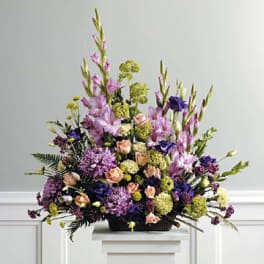 Large mixed floral arrangement in a low black container with purple, pink, and peach blooms