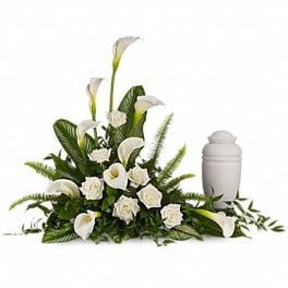 White funeral floral arrangement with calla lilies and roses beside an urn