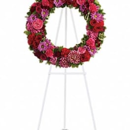 Circular floral wreath on a white easel with red and pink blooms