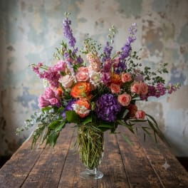 Mixed bouquet of pink, purple, and orange flowers in a clear glass vase