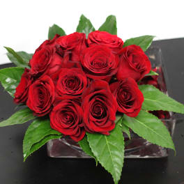Compact arrangement of red roses in a clear glass cube vase