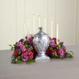 Pink and purple floral arrangement with tall white candles around a silver urn