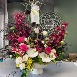 Large floral arrangement with orchids, roses, and tulips in a white pedestal vase