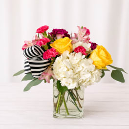 Bouquet of yellow roses, white hydrangea, and pink flowers in a glass vase