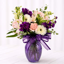 Mixed bouquet of pink, purple, and white flowers in a purple glass vase