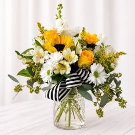 Sunflower and white daisy bouquet in a glass vase with a striped ribbon