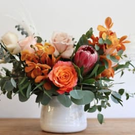 Low arrangement of orange and blush flowers in a white ceramic pot