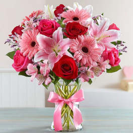 Bouquet of pink and red flowers in a clear glass vase with a pink ribbon