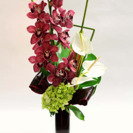 Tall orchid arrangement in a glass vase with burgundy and white blooms
