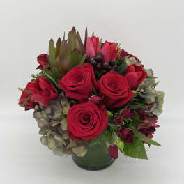Low round arrangement of red roses with mixed hydrangeas in a glass vase