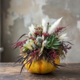 Floral arrangement in a yellow pumpkin-shaped container with white and burgundy accents
