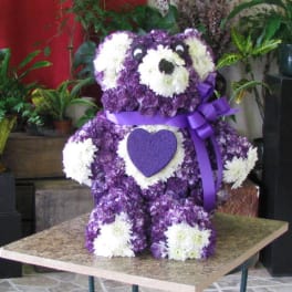 Purple and white teddy bear made of flowers with a ribbon bow